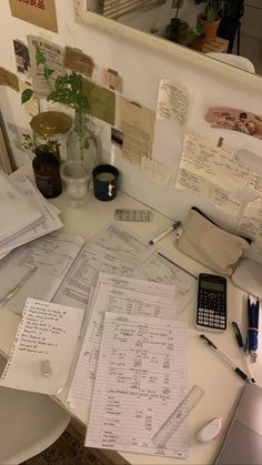 a cluttered desk with papers and calculator on it in front of a mirror