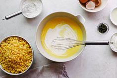 bowls filled with corn, eggs and other ingredients on a white counter top next to an egg whisk