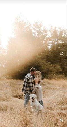 a man and woman standing in tall grass with their dog