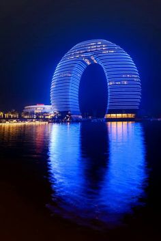 the building is lit up at night with bright lights on it's sides and reflecting in the water