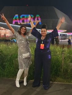 two women standing next to each other in front of a building with lights on it