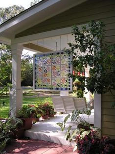 a porch with potted plants and a quilt hanging from the side of it's wall