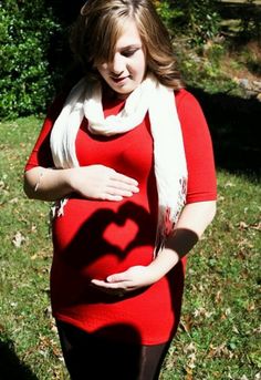 a pregnant woman is standing in the grass with her hands on her belly, casting a heart shaped shadow