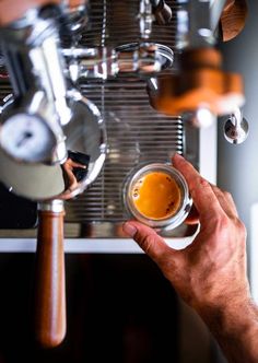 a person is holding a glass in front of a espresso machine with liquid coming out of it