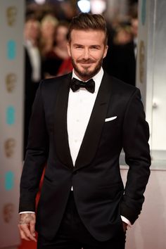 a man in a tuxedo and bow tie standing on a red carpet at an event