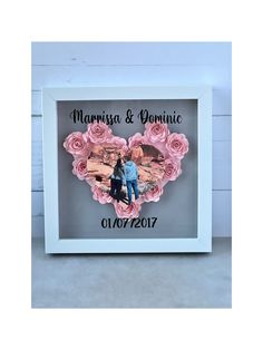 a white frame with pink roses in the shape of a heart and an image of two people