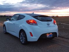 a white car is parked on the side of the road at sunset or dawn with clouds in the sky