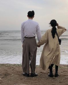 a man and woman holding hands while standing on top of a beach next to the ocean