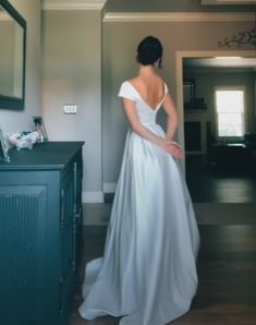 a woman in a white dress is standing near a dresser