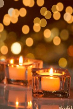 three lit candles sitting on top of a table with blurry lights in the background