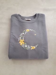 a gray t - shirt with yellow flowers and a crescent on the front that says c