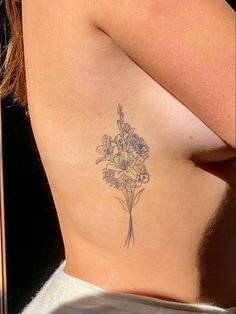 a woman's lower back tattoo with flowers on her left side ribcage