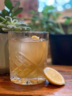 a glass filled with lemonade sitting on top of a wooden table next to a potted plant