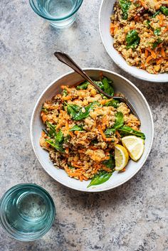 two bowls filled with rice and vegetables on top of a table next to water glasses