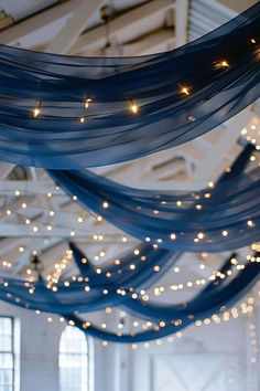 the ceiling is decorated with blue sheer fabric and fairy lights hanging from it's rafters