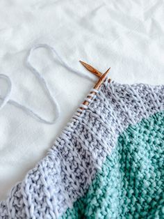 a close up of a knitted blanket on a bed with two knitting needles next to it