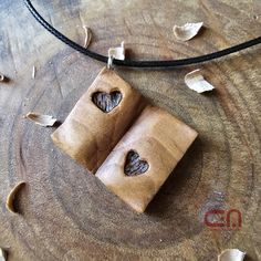 two pieces of wood with holes in them on a leather cord necklace hanging from a tree stump