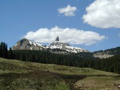 the mountains are covered with snow and trees in the foreground is a stream running through it