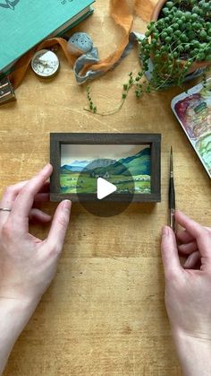 two hands holding scissors over a wooden table with pictures and other items on the table