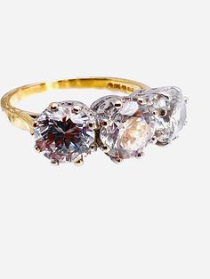 three stone ring on white background with gold band and two diamonds in the middle, all surrounded by smaller stones