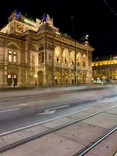 an old building is lit up at night with street lights in the foreground and cars driving by