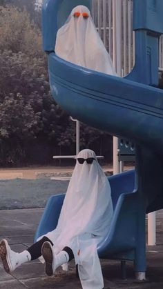 a man in a ghost costume sitting on a slide at a playground with his feet propped up