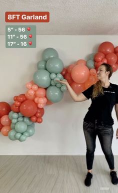 a woman is standing in front of balloons and pointing to the wall with her hand