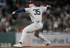 a baseball player pitching a ball on top of a field with people in the background