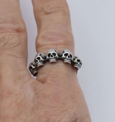 Welcome to our Shop! Five small skulls are set together on the top of the band, to comfortably lay upon finger. This band has been hand carved in wax, cast into sterling silver, and finally meticulously refined and polished to perfection.  Ring is made for you in any size. We use American measurement. Please don't hesitate to contact us further  with any enquire. Thanks for stopping by! Adjustable Skull Print Ring For Halloween, Edgy Silver Skull Ring For Gift, Adjustable Symbolic Skull Ring, Adjustable Punk Skull Ring, Handmade Gothic Sterling Silver Skull Ring, Silver Punk Skull Ring, Handmade Silver Skull Ring, Symbolic Style, Hand-cast Sterling Silver Black Skull Ring, Small Skull