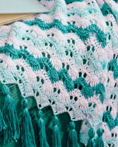 a green and white crocheted blanket with tassels