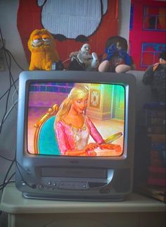 there is a small television with a barbie doll on it's screen and some stuffed animals in the background