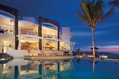 an outdoor swimming pool next to a large white building at night with palm trees in the foreground