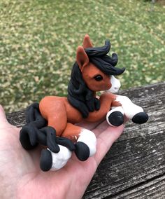 a small toy horse sitting on top of someone's hand in front of some grass