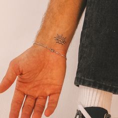 a person's hand with a small sun tattoo on their left wrist, and a chain around the wrist