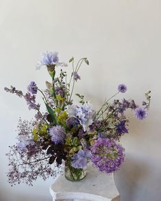 a vase filled with purple and white flowers sitting on top of a marble table next to a wall