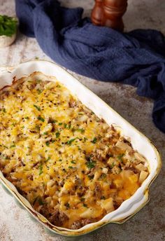 a casserole dish with meat and cheese in it sitting on a table next to a blue towel