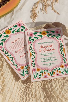 two wedding cards sitting on top of a table next to a slice of watermelon