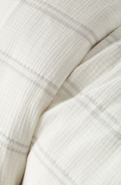 an unmade bed with white linens and plaid pattern on the comforter cover