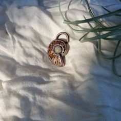 a piece of jewelry sitting on top of a white sheet next to some plants and grass