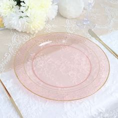 a pink plate with gold trim sits on a white lace tablecloth next to flowers