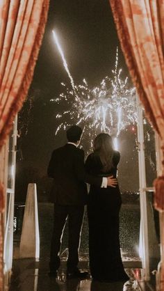 a man and woman standing in front of a firework display with their arms around each other