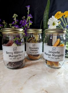 three jars filled with different types of spices on a marble counter top next to flowers