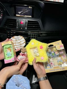 two hands are holding small stuffed animals in front of a car dashboard with other toys