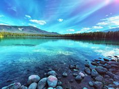 a lake surrounded by rocks and trees under a blue sky