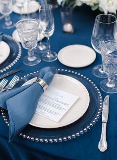 a blue table cloth with silver beaded edges and place settings on it is set for a formal dinner