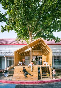 children are playing on a wooden structure in front of a building that is made out of wood