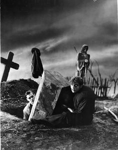 an old black and white photo of two men sitting in front of a cross on the ground