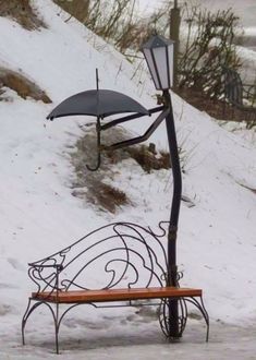 a bench with an umbrella attached to it in the snow next to a street light