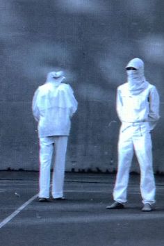 two men in white suits standing next to each other on a tennis court with one holding a racket