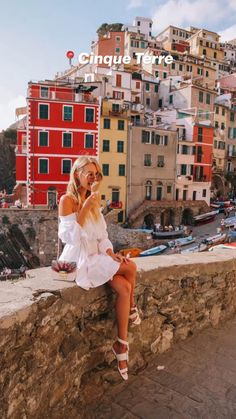 a woman is sitting on a wall talking on her cell phone in front of some buildings